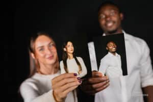 Two people holding printed professional headshots captured by Lumen Activations, showcasing clean studio portraits on a black background.