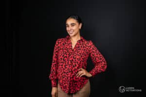 A woman smiling in a red patterned blouse during a professional studio headshot session with Lumen Activations.